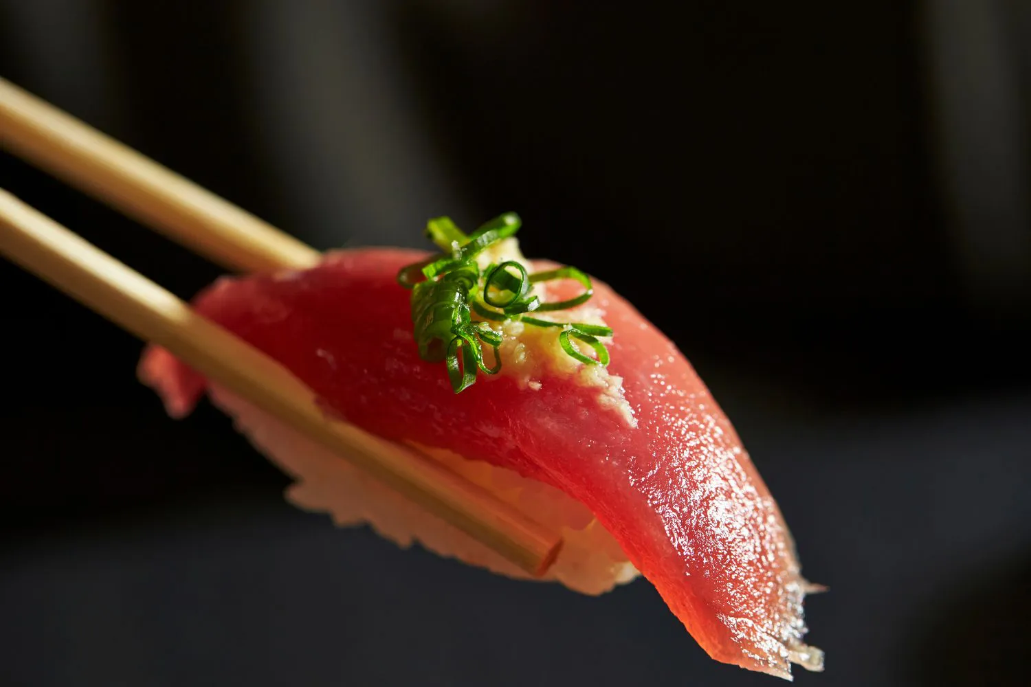 Tuna nigiri with scallion garnish held by chopsticks at Takora, a Japanese Restaurant in Houston